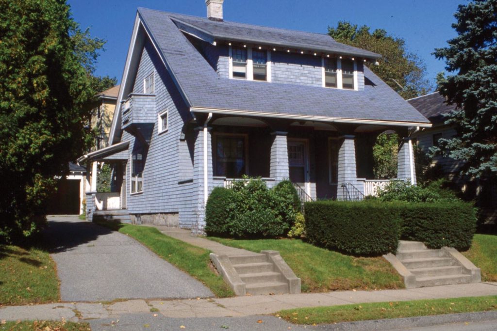 This bungalow has a wood shingle exterior with strong battered porch columns and a low slung dormer. 