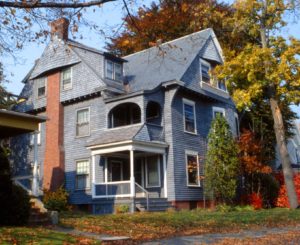 This large Shingle style house has a unique exterior chimney that dives through the gable end shingles.